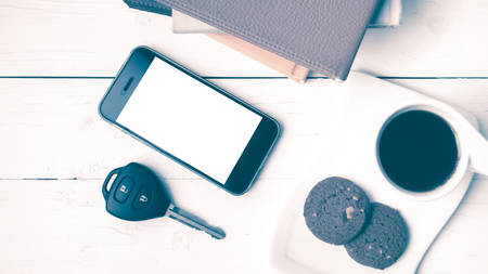 coffe cup with cookie,phone,car key and stack of book on white wood table vintage styleの写真素材