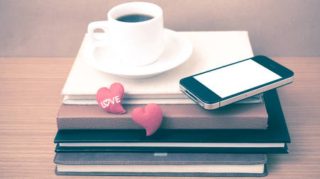 coffee,phone,stack of book and heart on wood table background vintage styleの写真素材