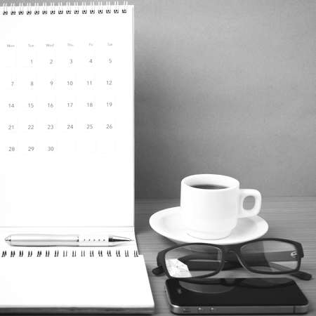 coffee,phone,eyeglasses,notepad and canlendar on wood table background black and white colorの写真素材