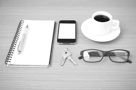 coffee,phone,notepad,eyeglasses and key on wood table background black and white color