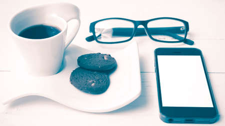 coffee cup with cookie,phone and eyeglasses on white wood table vintage styleの写真素材