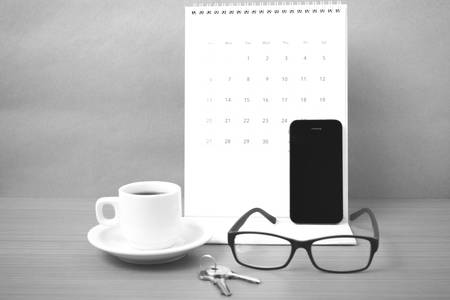 coffee,phone,eyeglasses,calendar and key on wood table background black and white colorの写真素材