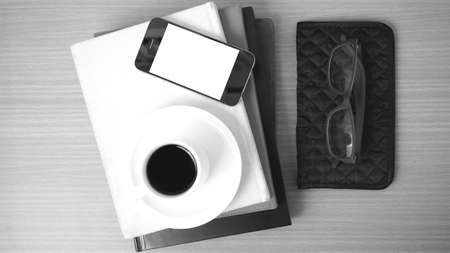 coffee,phone,eyeglasses,stack of book and wallet on wood table background black and white colorの写真素材