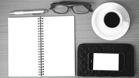 coffee,phone,eyeglasses,notepad and wallet on wood table background black and white colorの写真素材