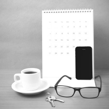 coffee,phone,eyeglasses,calendar and key on wood table background black and white colorの写真素材