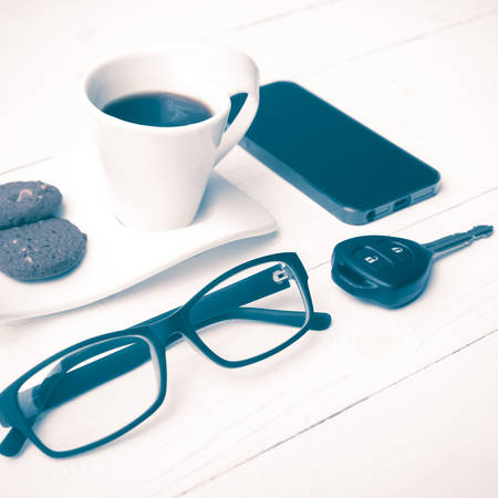 coffee cup with cookie,phone,eyeglasses and car key on white wood table vintage style