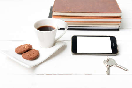 coffee cup with cookie,phone,stack of book and key on white wood tableの写真素材