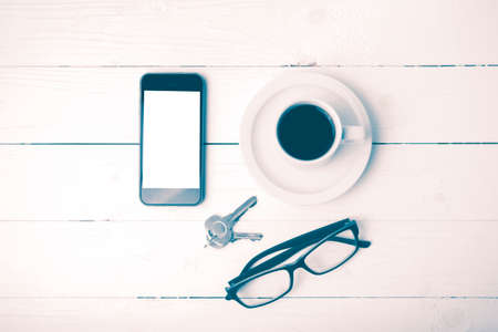 coffee cup with phone, eyeglasses and key on white wood table vintage style