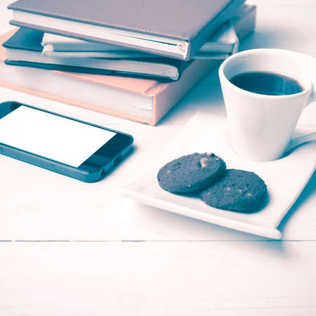 coffe cup with cookie,phone and stack of book on white wood table vintage style