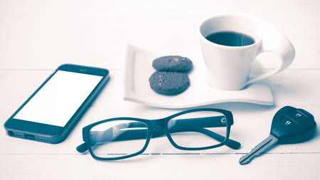 coffee cup with cookie,phone,eyeglasses and car key on white wood table vintage style
