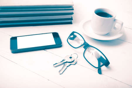 coffee cup with phone,key,eyeglasses and stack of book on white wood table vintage styleの写真素材