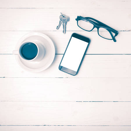 coffee cup with phone, eyeglasses and key on white wood table vintage styleの写真素材