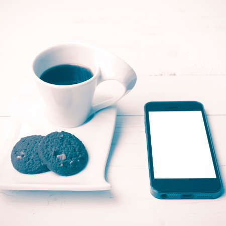 coffee cup with cookie and phone on white wood background vintage style