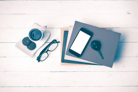 coffe cup with cookie,phone,car key,eyeglasses and stack of book on white wood table vintage style