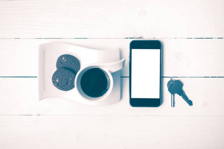 coffee cup with cookie,phone and key on white wood table vintage styleの写真素材