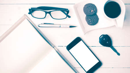 coffee cup with cookie,phone,open notebook,car key and eyeglasses on white wood table vintage styleの写真素材