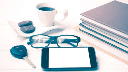 coffe cup with cookie,phone,car key,eyeglasses and stack of book on white wood table vintage styleの写真素材