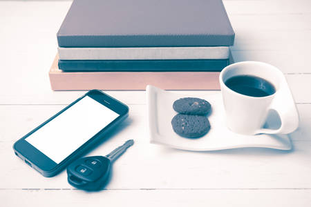 coffe cup with cookie,phone,car key and stack of book on white wood table vintage styleの写真素材