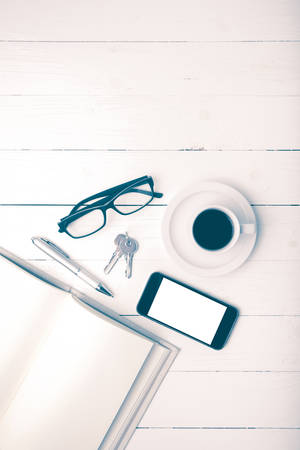 coffee cup with phone, key,eyeglasses and open notebook on white wood table vintage styleの写真素材