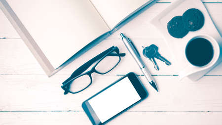 coffee cup with cookie,phone,open notebook and eyeglasses on white wood table vintage styleの写真素材
