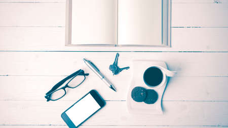 coffee cup with cookie,phone,open notebook and eyeglasses on white wood table vintage styleの写真素材