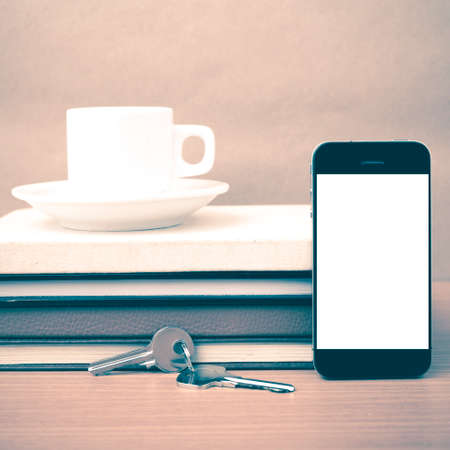 coffee cup with phone key and stack of book on wood background vintage style