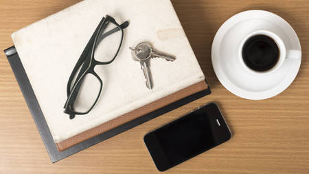 coffee,phone,key,eyeglasses and stack of book on wood table background