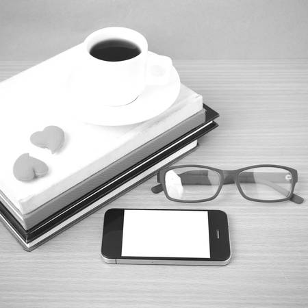 coffee,phone,eyeglasses,stack of book and heart on wood table background black  and white colorの写真素材