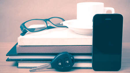 coffee,phone,car key,eyeglasses and stack of book on wood table background vintage styleの写真素材