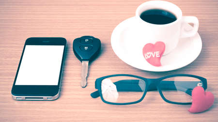 coffee,phone,eyeglasses,car key and heart on wood table background vintage styleの写真素材