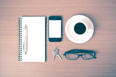 coffee,phone,notepad,eyeglasses and key on wood table background vintage styleの写真素材
