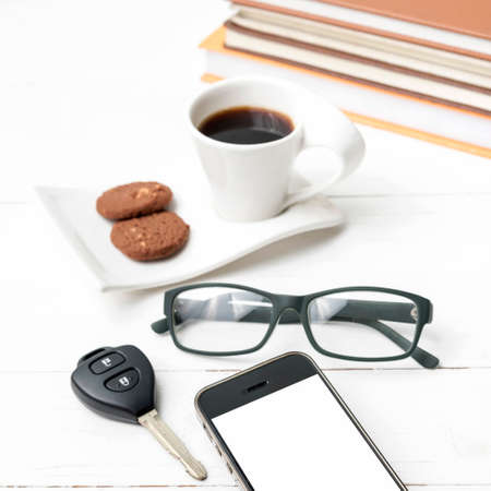 coffe cup with cookie,phone,car key,eyeglasses and stack of book on white wood tableの写真素材