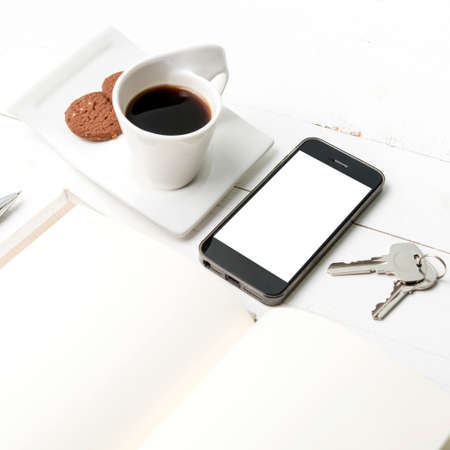coffee cup with cookie,phone,notebook and key on white wood tableの写真素材
