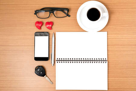 office desk : coffee and phone with car key,eyeglasses,notepad,heart on wood backgroundの写真素材