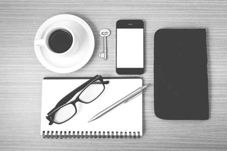 coffee and phone with notepad,key,eyeglasses and wallet on wood table background black and white colorの写真素材