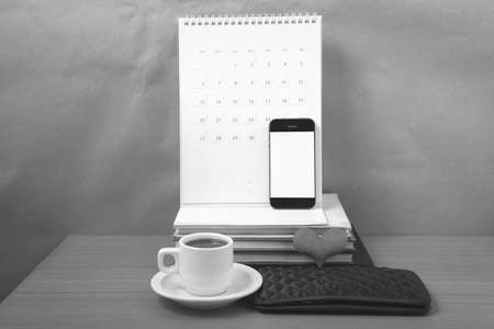 office desk : coffee with phone,wallet,calendar,heart,stack of book on wood background black and white colorの写真素材
