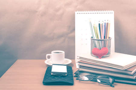 office desk : coffee with phone,wallet,calendar,color pencil box,stack of book,heart,eyeglasses on wood background vintage styleの写真素材