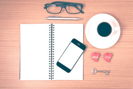 office desk : coffee and phone with key,eyeglasses,notepad,heart on wood background vintage styleの写真素材