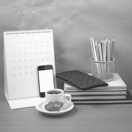 office desk : coffee with phone,wallet,calendar,heart,color pencil box,stack of book,heart on wood background black and white colorの写真素材