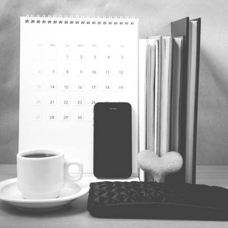 office desk : coffee with phone,wallet,calendar,heart,stack of book on wood background black and white colorの写真素材