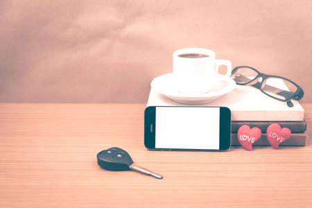 office desk : coffee and phone with car key,eyeglasses,stack of book,heart on wood background vintage styleの写真素材