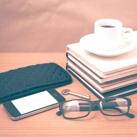 coffee and phone with stack of book,key,eyeglasses and wallet on wood background vintage style