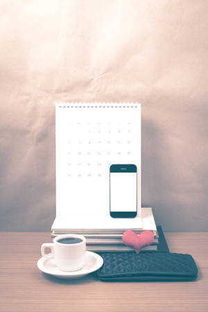 office desk : coffee with phone,wallet,calendar,heart,stack of book on wood background vintage styleの写真素材