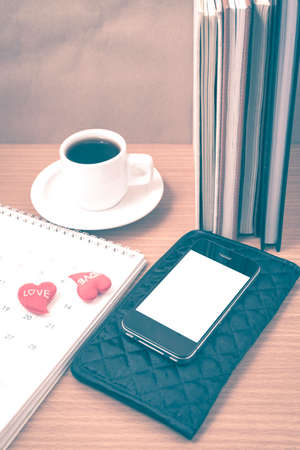 office desk : coffee with phone,wallet,calendar,heart,stack of book on wood background vintage styleの写真素材