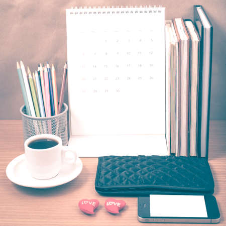 office desk : coffee with phone,wallet,calendar,heart,color pencil box,stack of book,heart on wood background vintage styleの写真素材