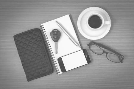 coffee and phone with notepad,car key,eyeglasses and wallet on wood table background black and white colorの写真素材