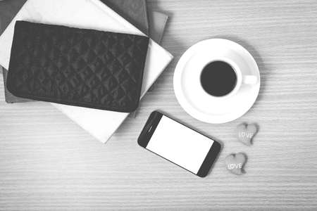 office desk : coffee with phone,stack of book,wallet on wood background black and white colorの写真素材