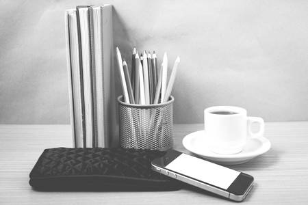 office desk : coffee with phone,stack of book,wallet,color box on wood background black and white...