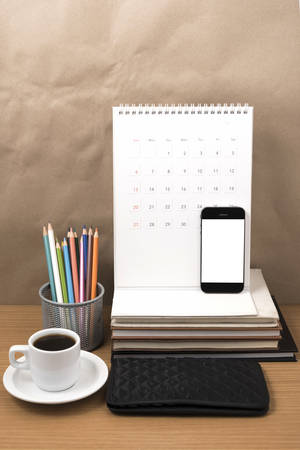 office desk : coffee with phone,wallet,calendar,color pencil box,stack of book on wood backgroundの写真素材