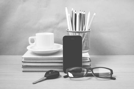 office desk : coffee and phone with car key,eyeglasses,stack of book,pencil box black and white...